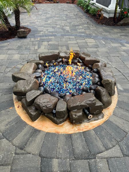 A fire pit with blue glass and flames, surrounded by stones, set on a stone patio.