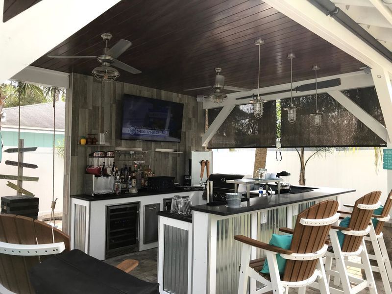 Outdoor bar with black countertop, bar stools, TV, ceiling fans, and dark wood ceiling.