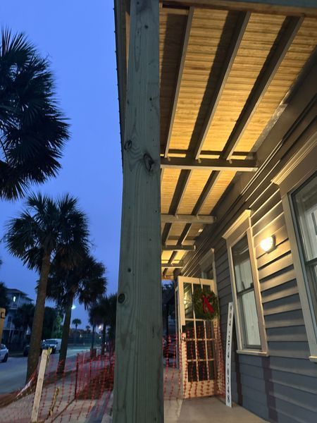 Exterior view of a building with a porch, lit from below. Palm trees line the street. A door with a wreath is open.