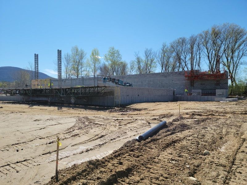 Construction site: industrial building under construction, workers, dump truck, gravel and dirt.