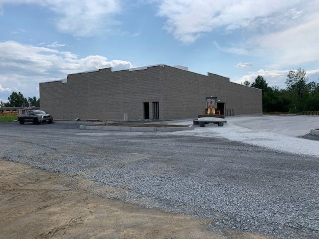 Building under construction, gray brick exterior, with a gravel parking lot and construction equipment.