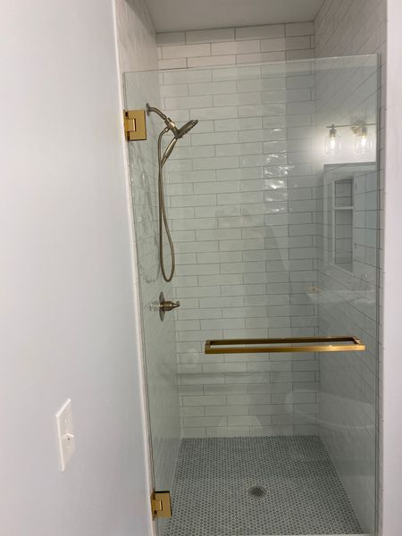 Shower with clear glass door, gold hardware, subway tile, and dark gray mosaic floor.
