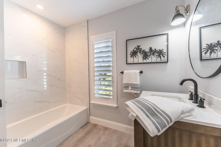 Bathroom with glass shower, toilet with grab bars, dark wood floor, and blue vanity.