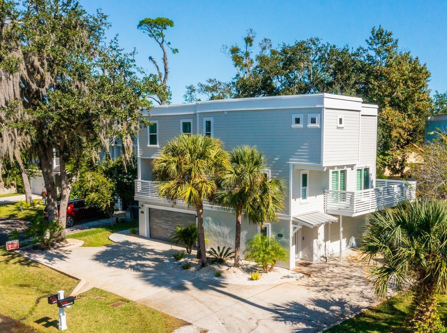 Modern two-story house with light gray siding and palm trees in front.