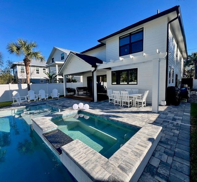 A two-story white house with a pool and patio. The sky is blue.
