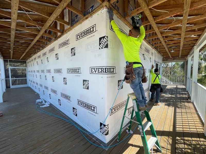 Construction workers installing siding on a building's exterior. One worker on a ladder, the other standing. Bright work clothes.