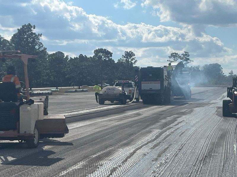 Road resurfacing: Asphalt paving equipment working on a road under a cloudy sky.