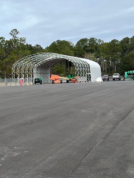 Metal arch structure under construction with vehicles and equipment in front.