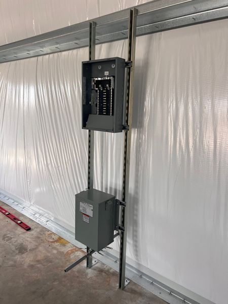 Electrical panel and transformer mounted on metal framing against a white wall.