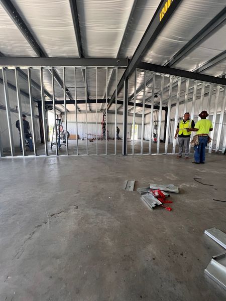 Interior of a construction site with steel frame walls, workers, and a concrete floor.