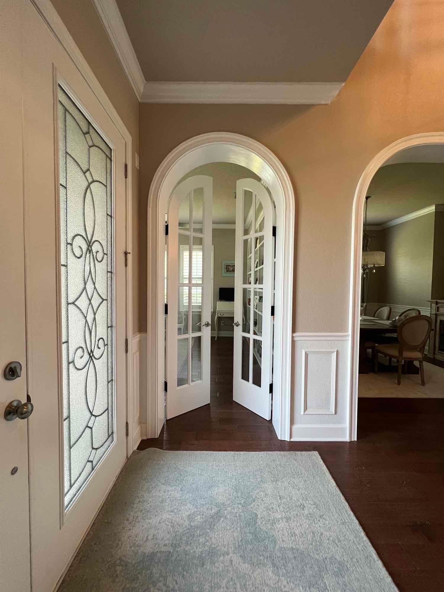 Entryway with white doors, stained glass, arched doorway, and a rug.