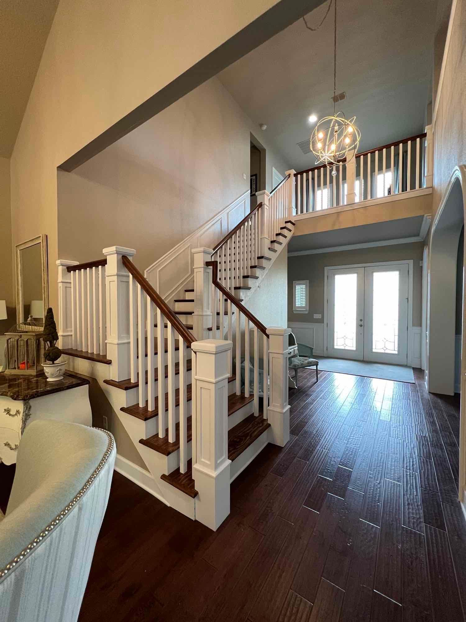 Staircase in a home with dark wood flooring, white banister and trim, and a chandelier.