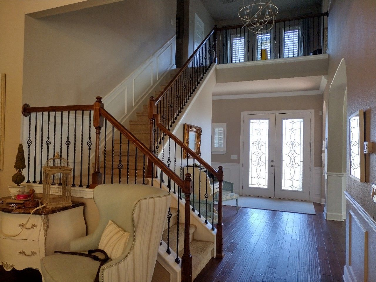 Entryway with staircase, stained wood railing, wrought iron balusters, double doors, and chandelier.
