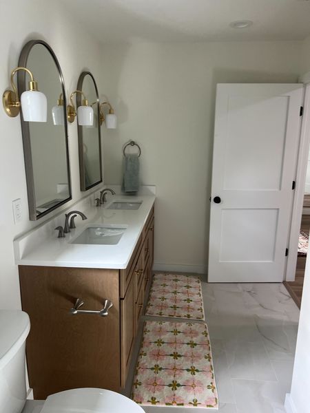 Bathroom with double vanity, arched mirrors, gold sconces, and a patterned runner rug.