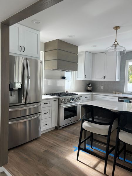 Modern white kitchen with stainless steel appliances, wood floors, and a light gray range hood.