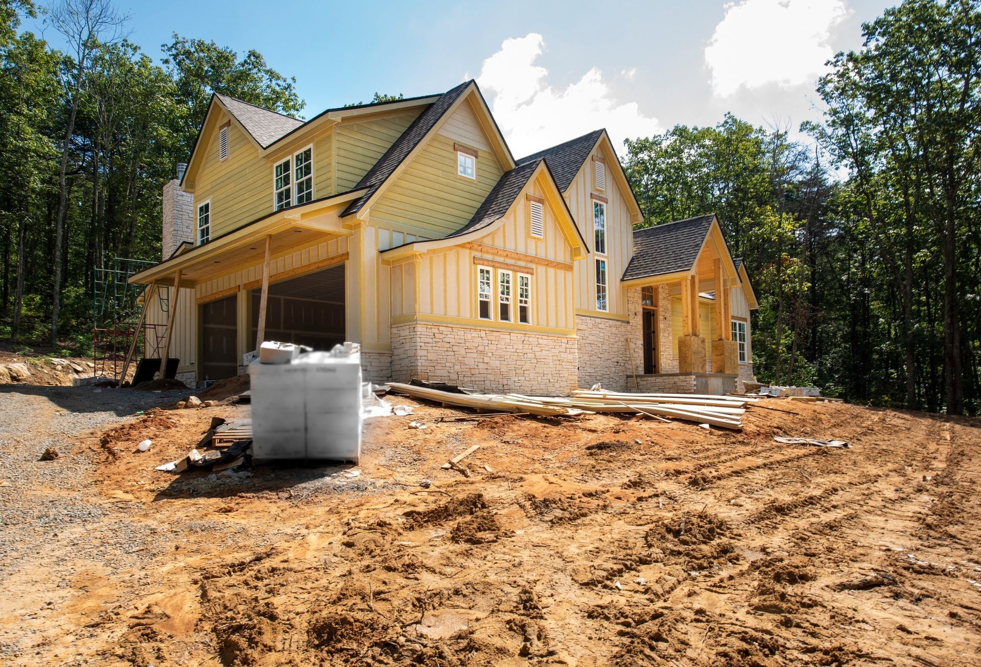 House under construction with beige siding, brick accents, and a wooded backdrop.