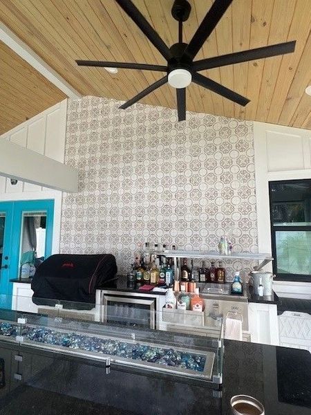 Modern bar with glass counter, bottles, and a black ceiling fan under a wood-paneled vaulted ceiling