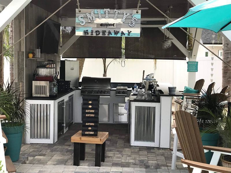 Outdoor bar under a canopy with a grill, stools, and lounge chairs