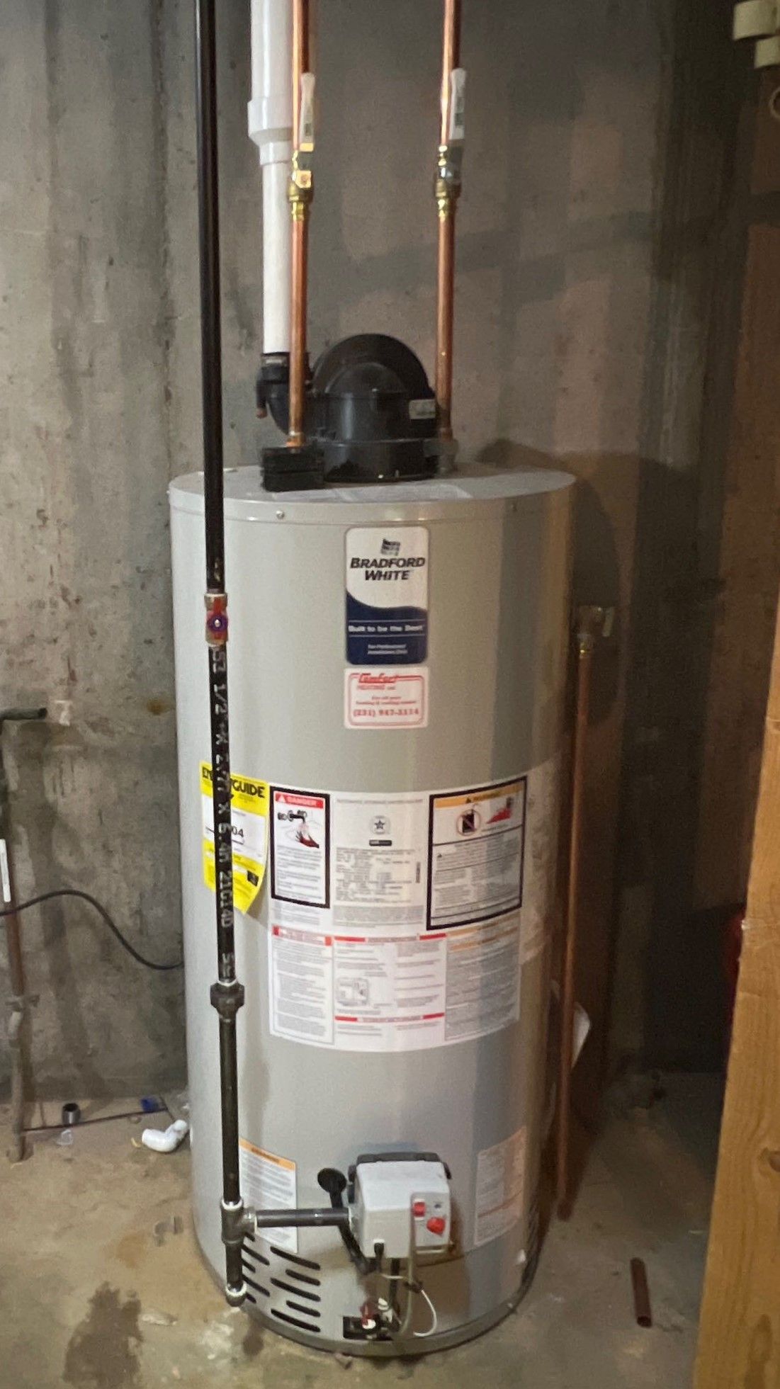 Water heater in a basement with copper pipes and a vent on top.