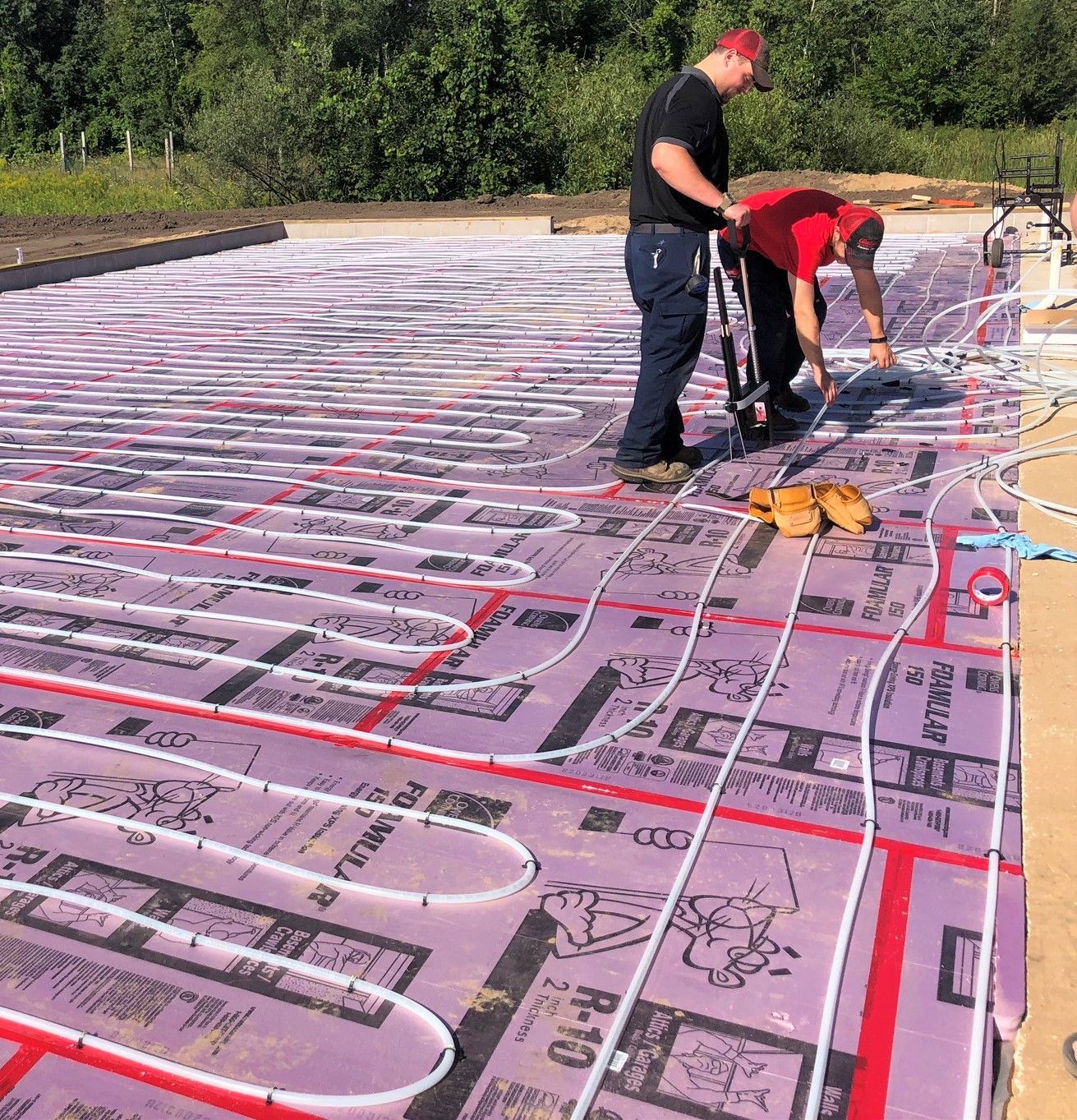 Workers installing tubing over pink insulation at a construction site outdoors