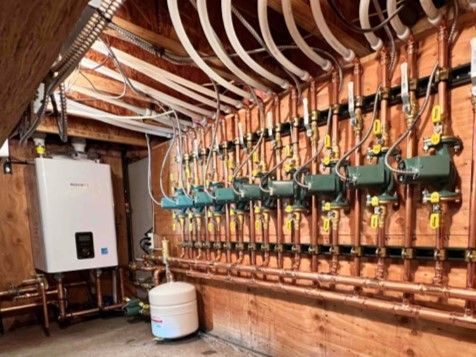 Hydronic heating manifold room with white control box, copper piping, and multiple green pump units