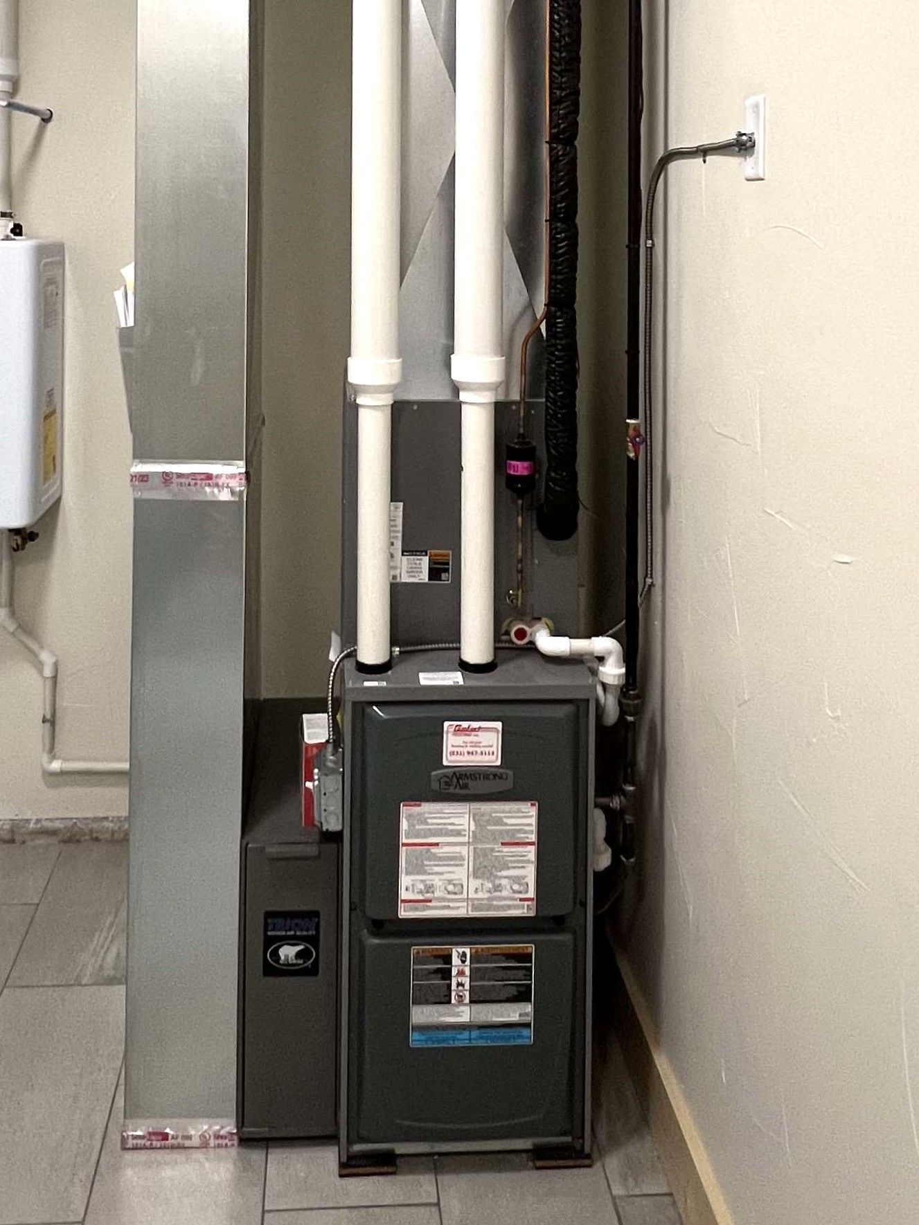 Furnace and HVAC ducts in a narrow utility alcove beside a wall.