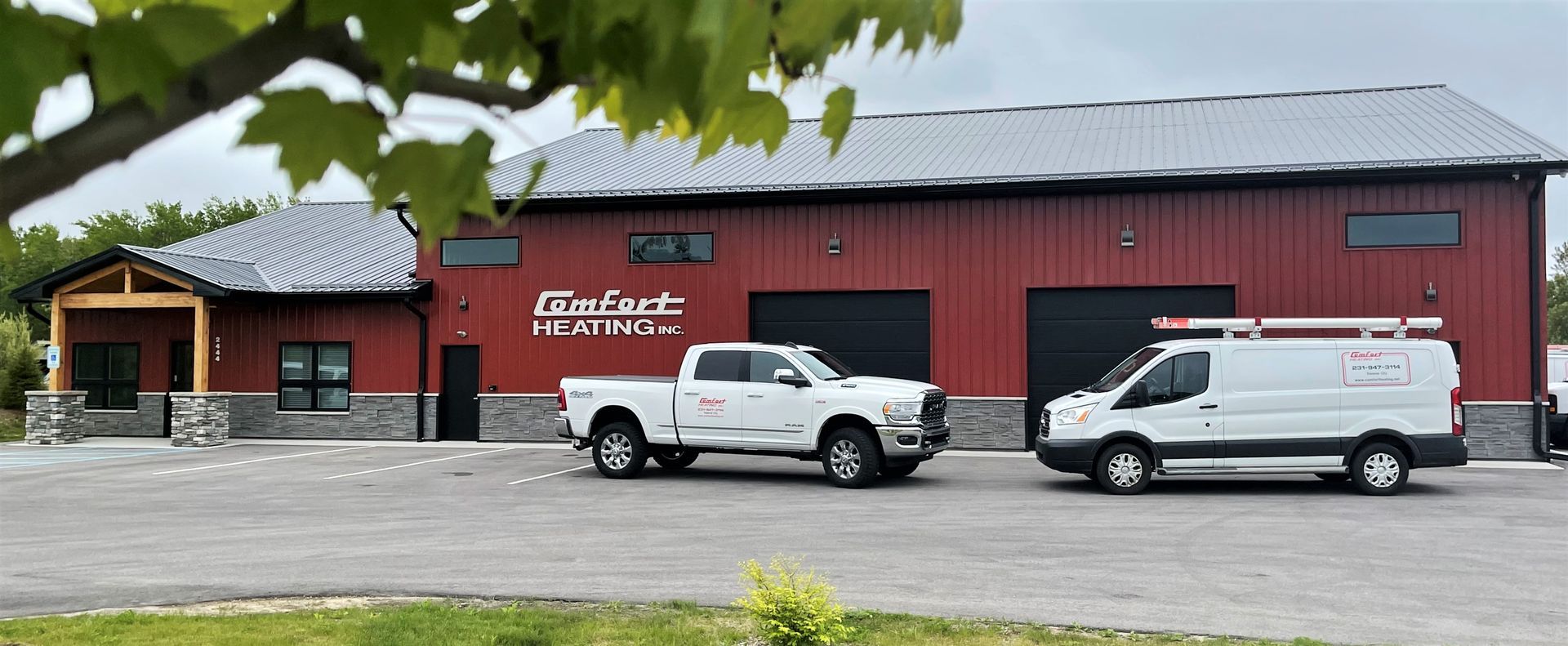 Red building with a gray roof, two white vehicles parked outside, and mountains in the background.
