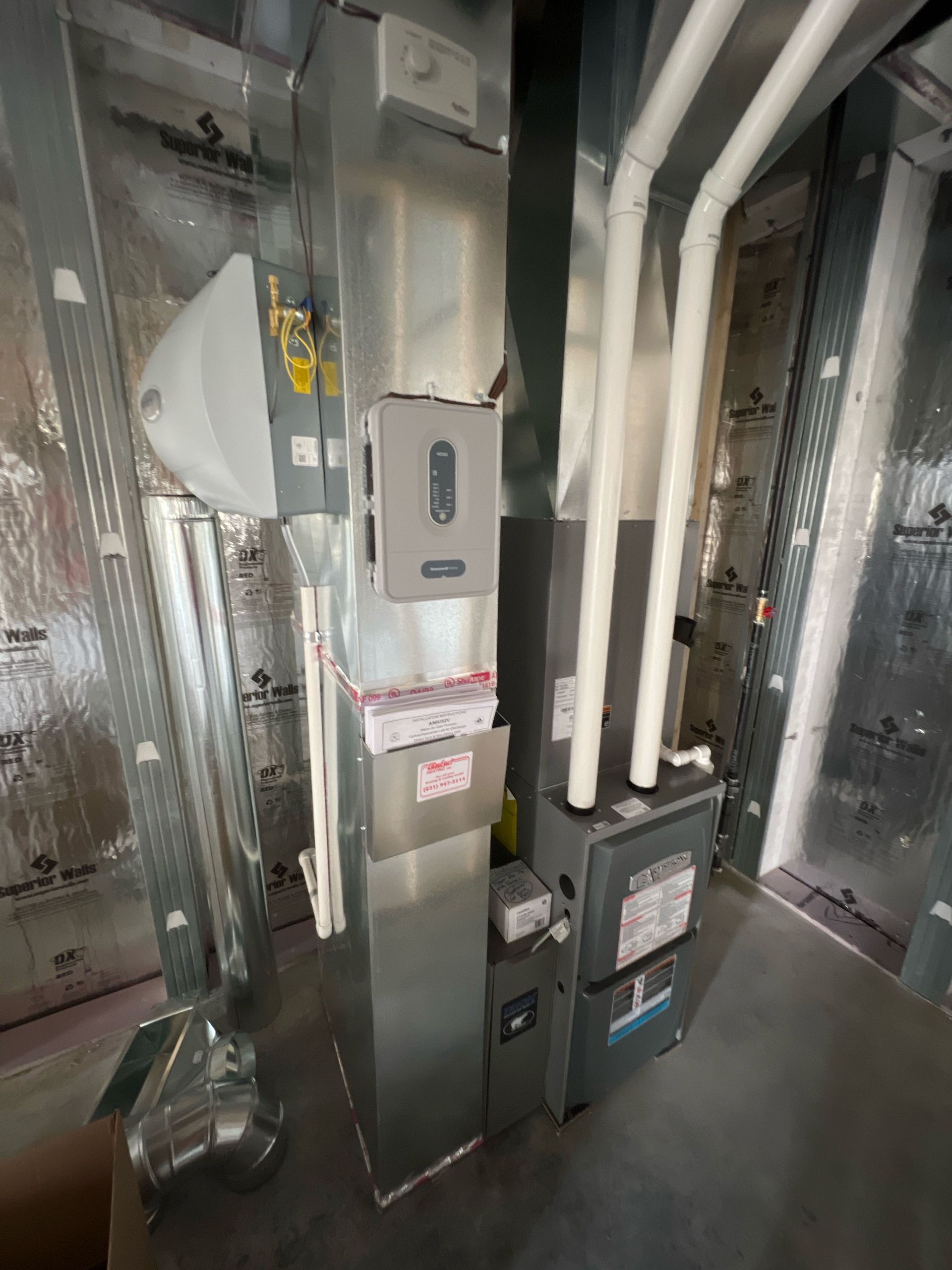 Basement utility room with HVAC ducts, pipes, and a furnace unit on a concrete floor.