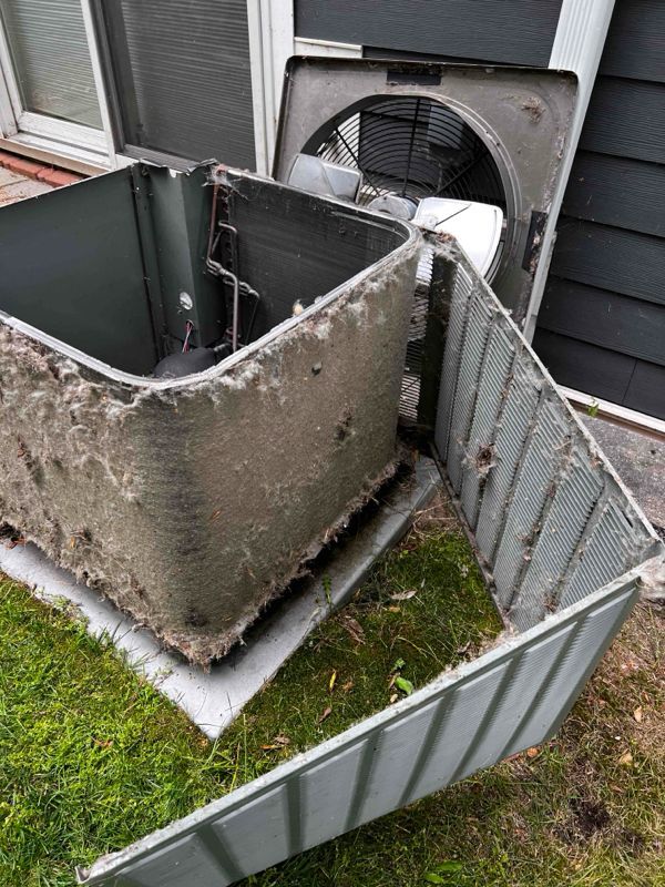 Damaged outdoor HVAC unit with bent metal panels beside a building and fence.
