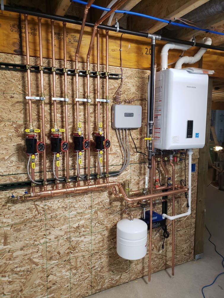 Residential plumbing and heating system with copper pipes, valves, white control units, and a wall-mounted boiler.