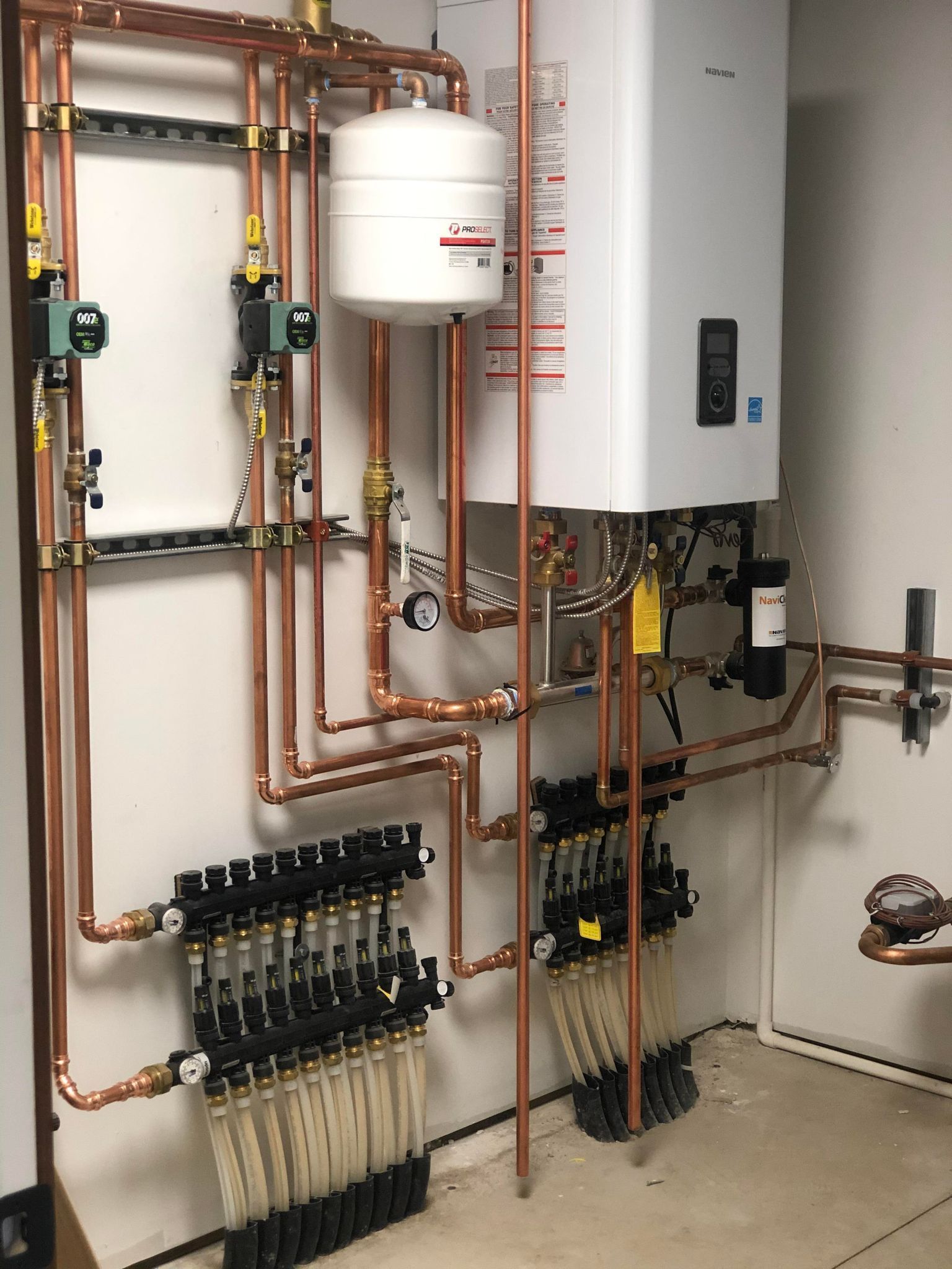Wall-mounted plumbing and heating system with copper pipes, manifolds, and a white boiler tank in a utility room