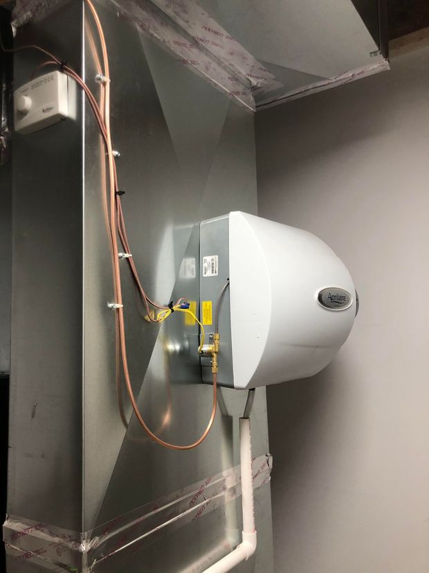 Wall-mounted white industrial fan in a gray utility room with exposed wiring and ductwork
