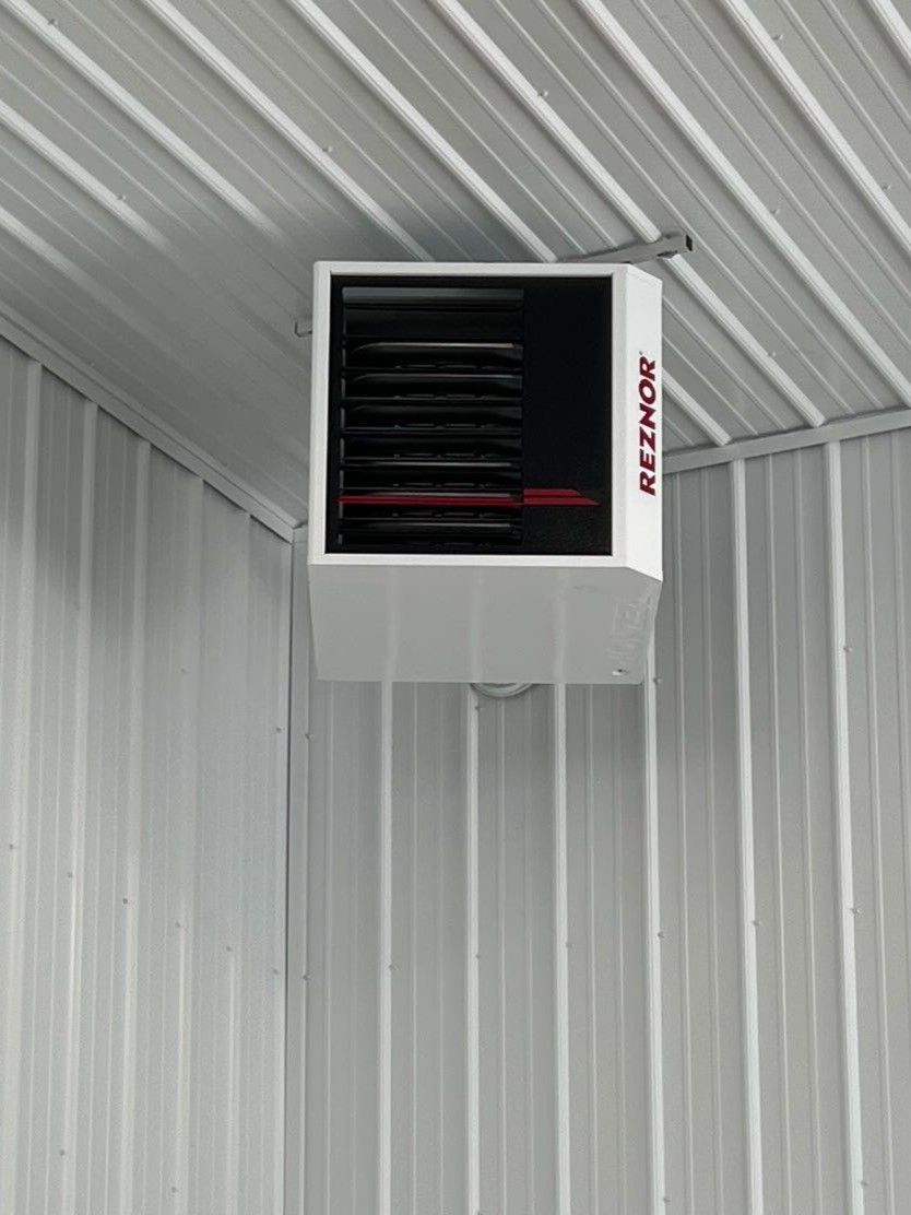 Wall-mounted white heater with black grille on a white corrugated metal ceiling and wall.