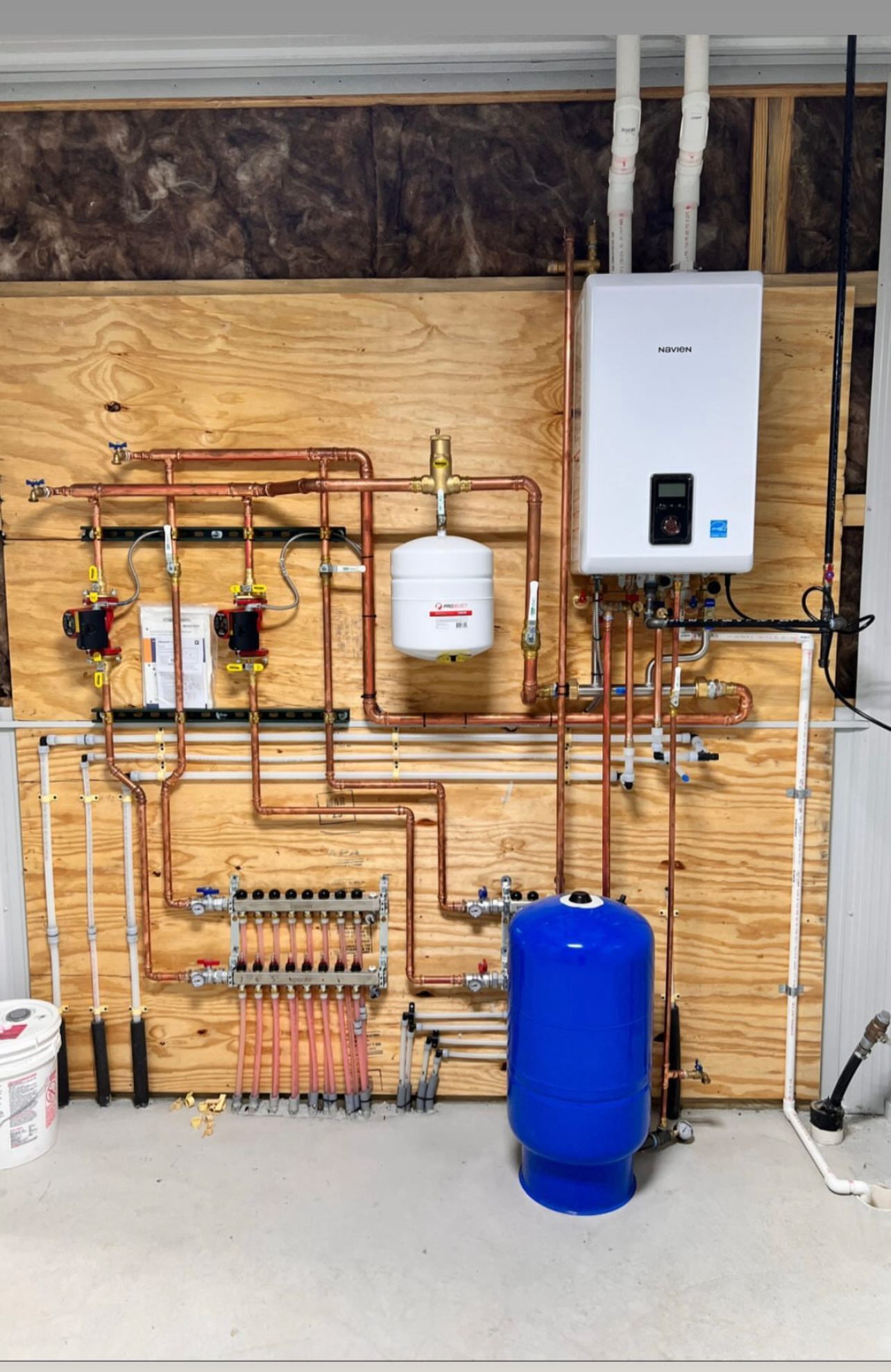 Wall-mounted plumbing and water filtration system with copper pipes, white unit, and blue tank in a utility room.