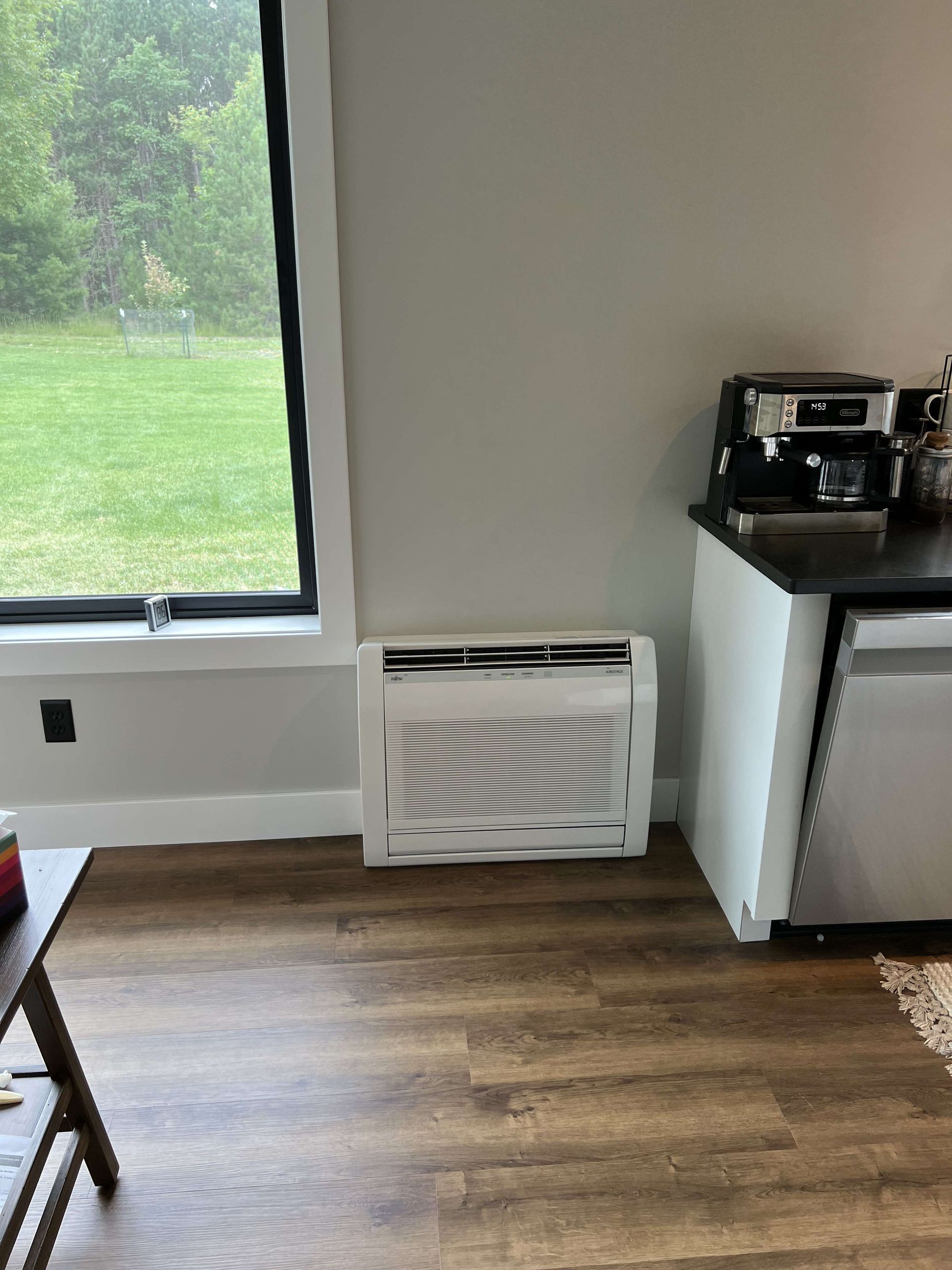 Bright room with wood floor, window, wall heater, and a coffee station on a counter.