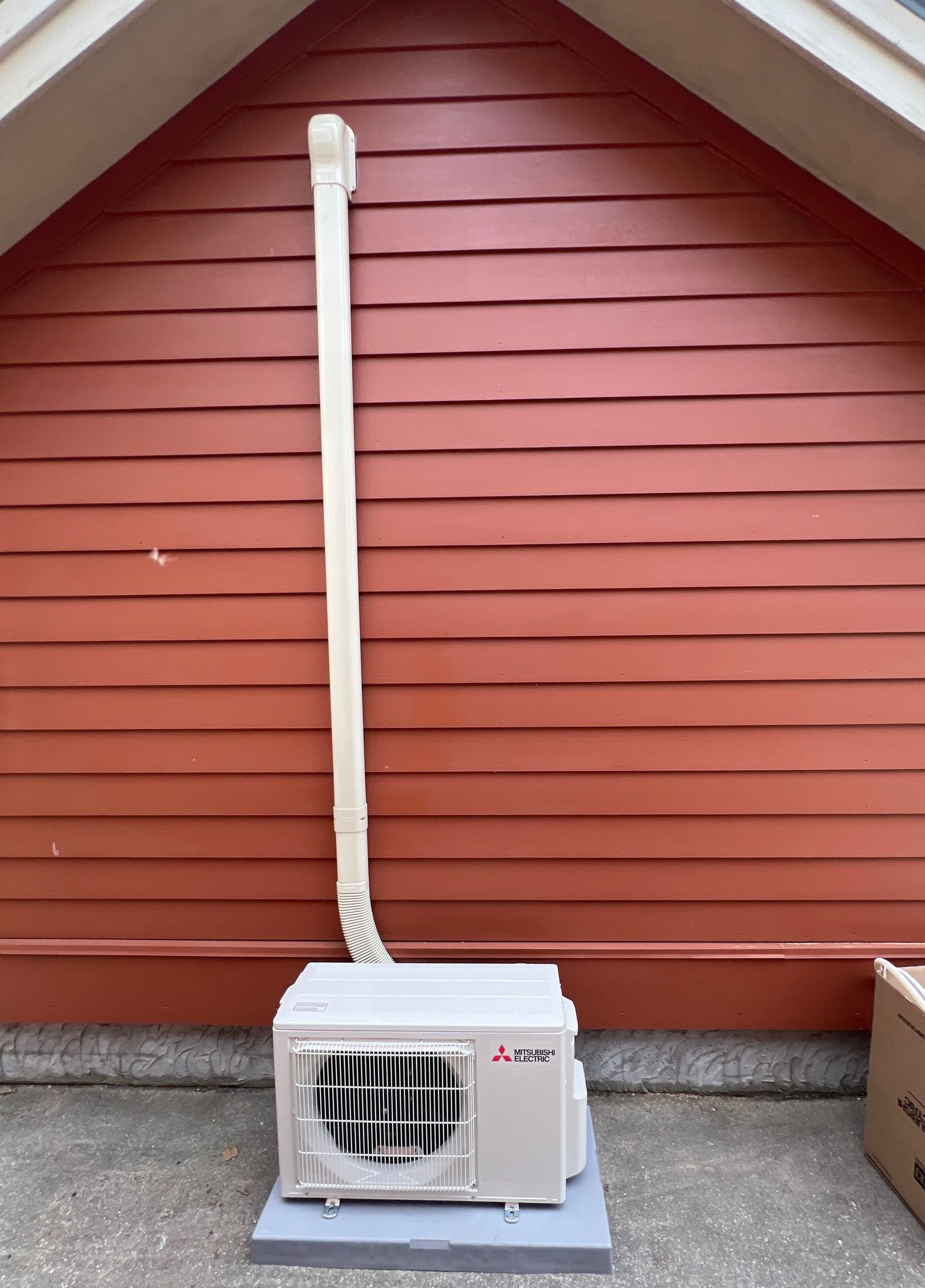 Outdoor HVAC unit beside red house siding with white vent pipe