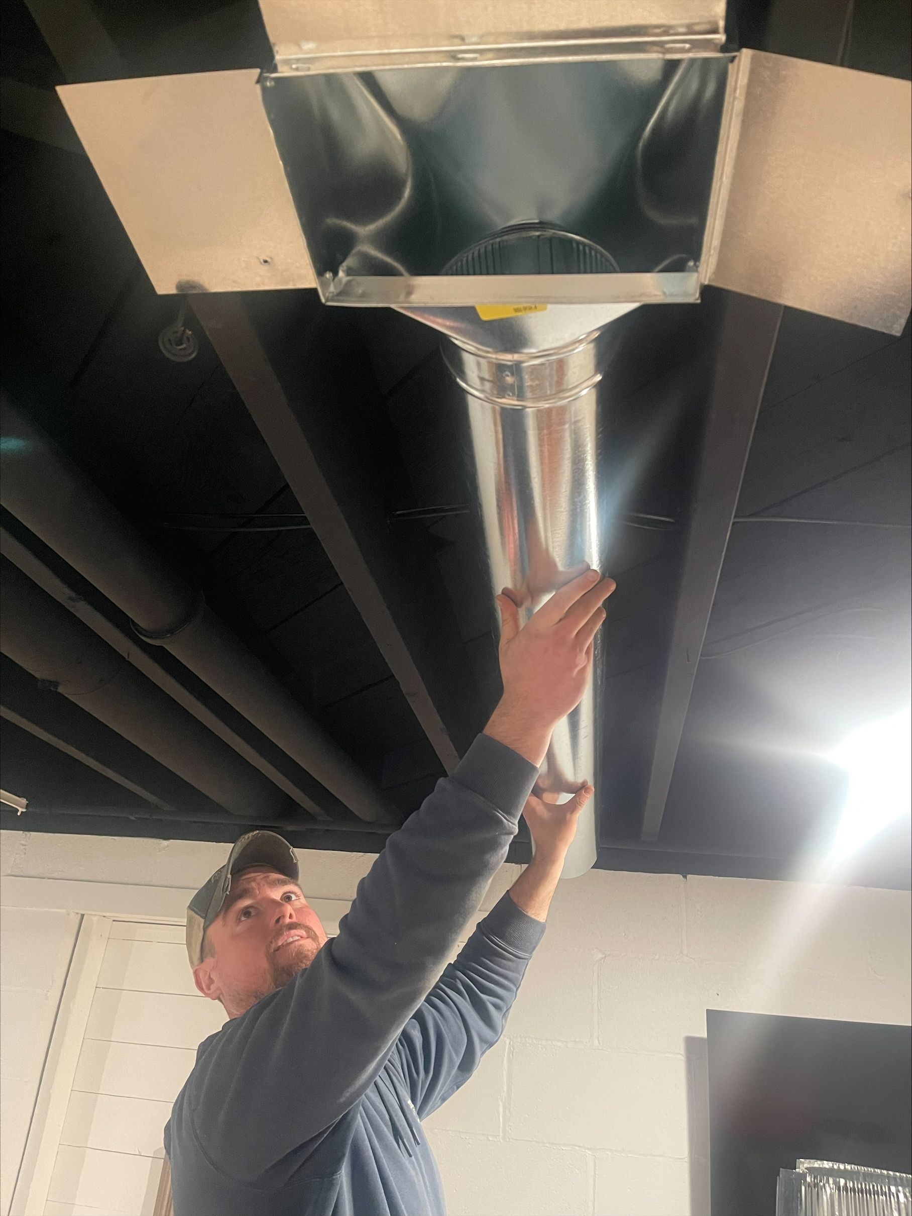 Worker installing shiny metal ducting in a ceiling space