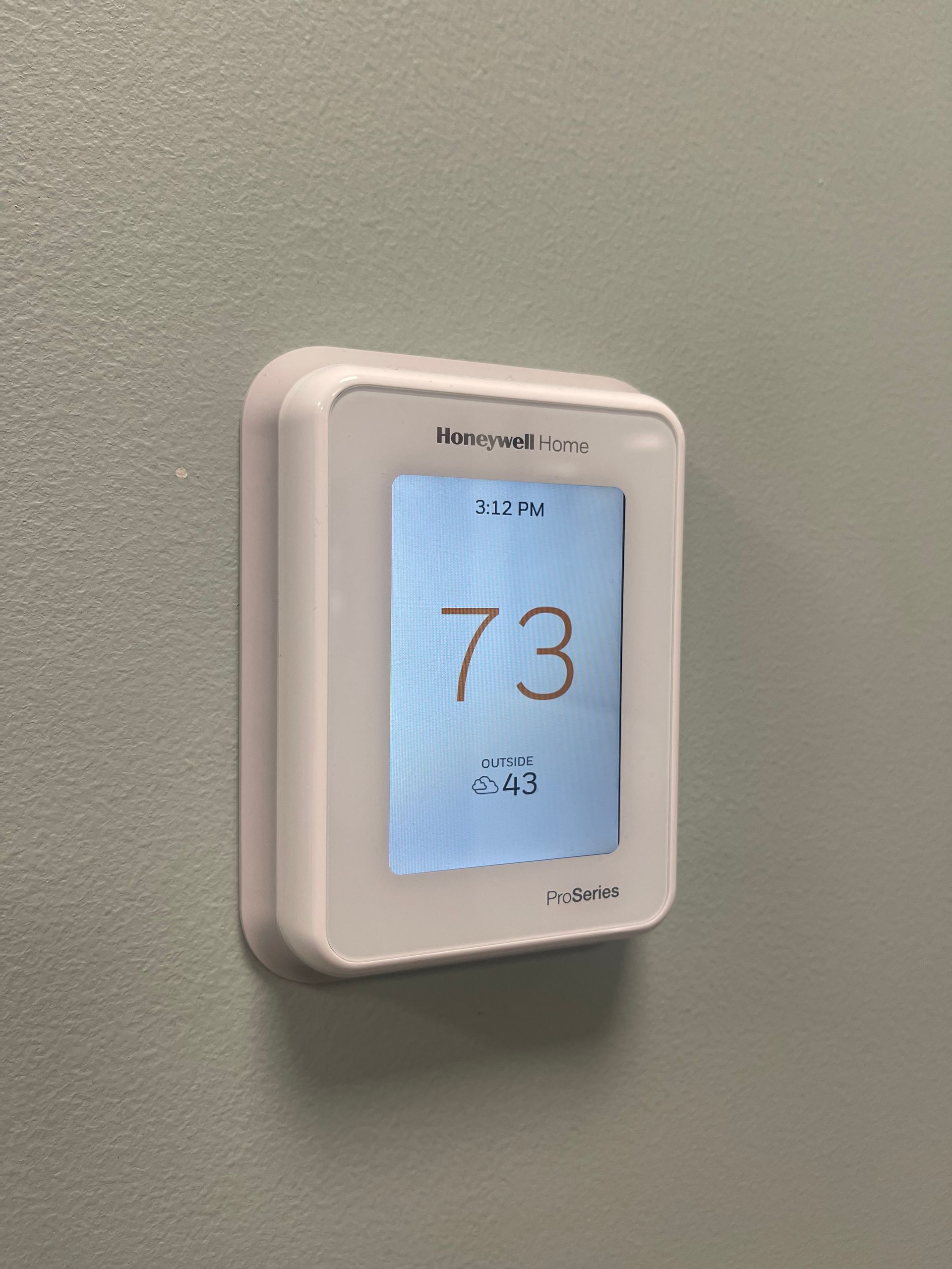 Wall-mounted digital thermostat displaying 73° on a gray wall