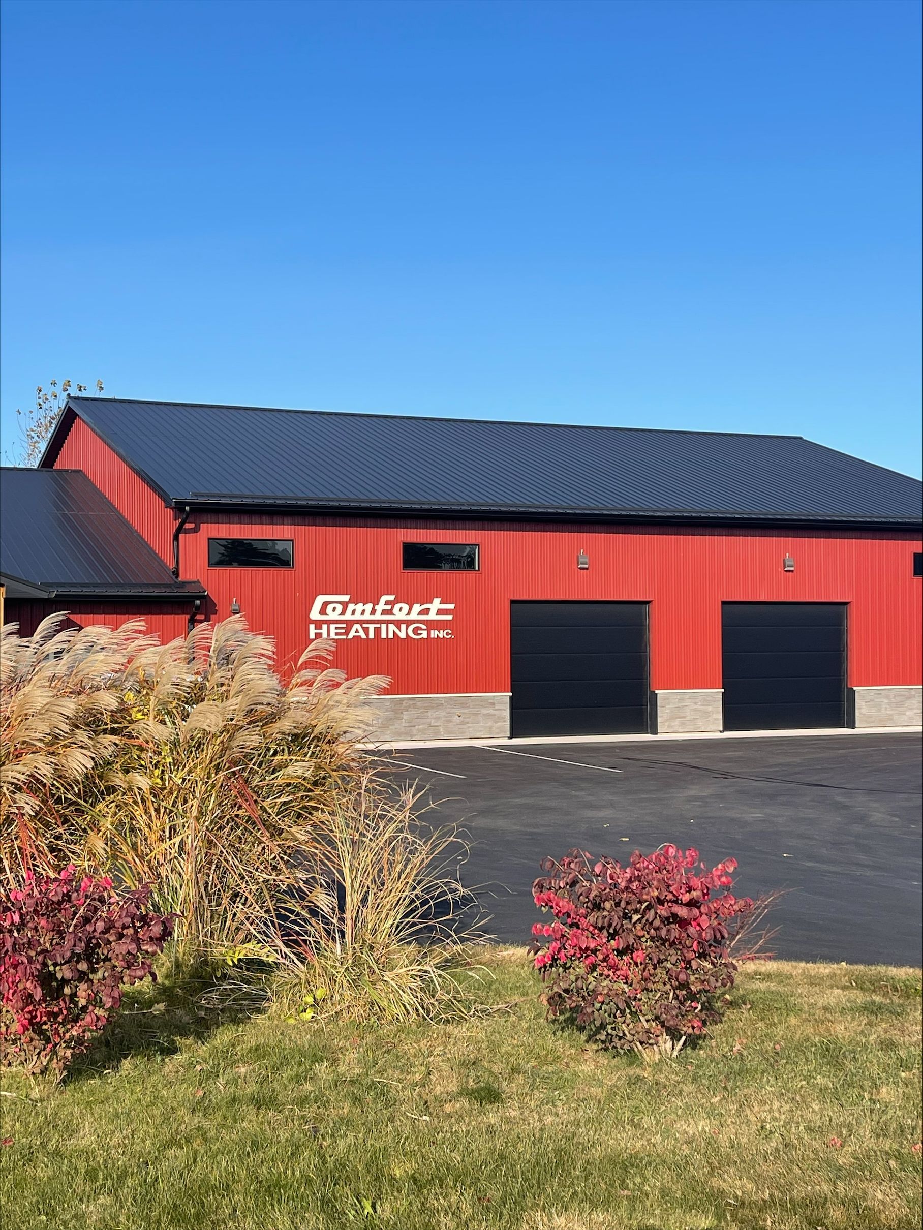Red barn-style commercial building with black roof and garage doors, red shrubs, and blue sky