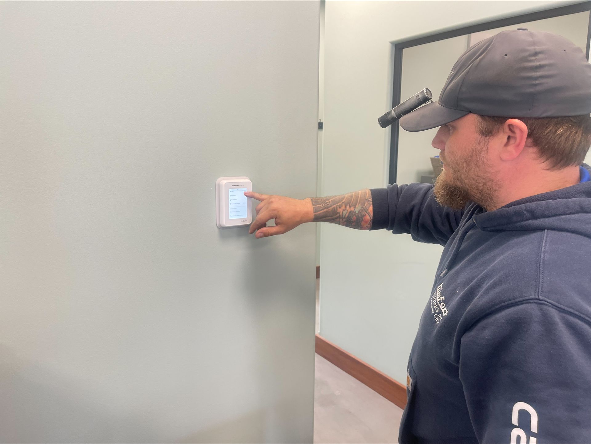 Man reaching to adjust a wall thermostat in a hallway with gray walls