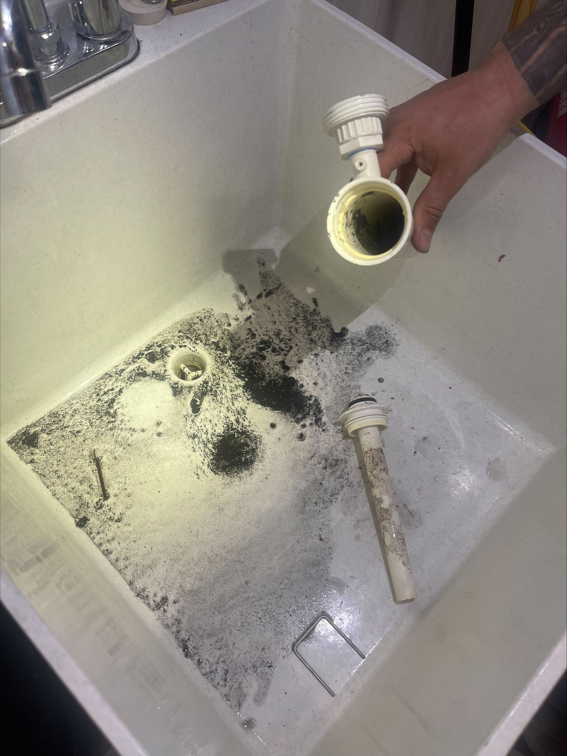 Hand holding a white PVC pipe over a trash bin with spilled black debris and a broken pipe inside