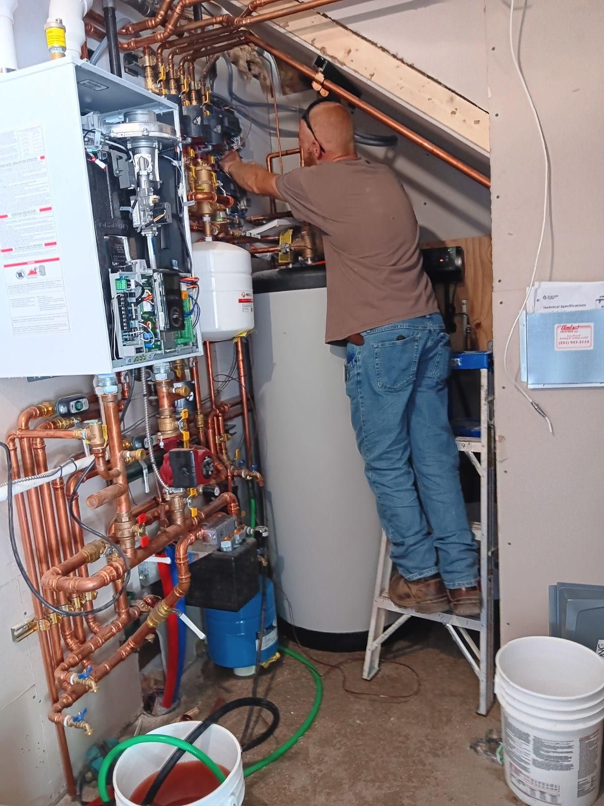 Technician standing on a step stool working on a boiler and exposed plumbing in a utility room