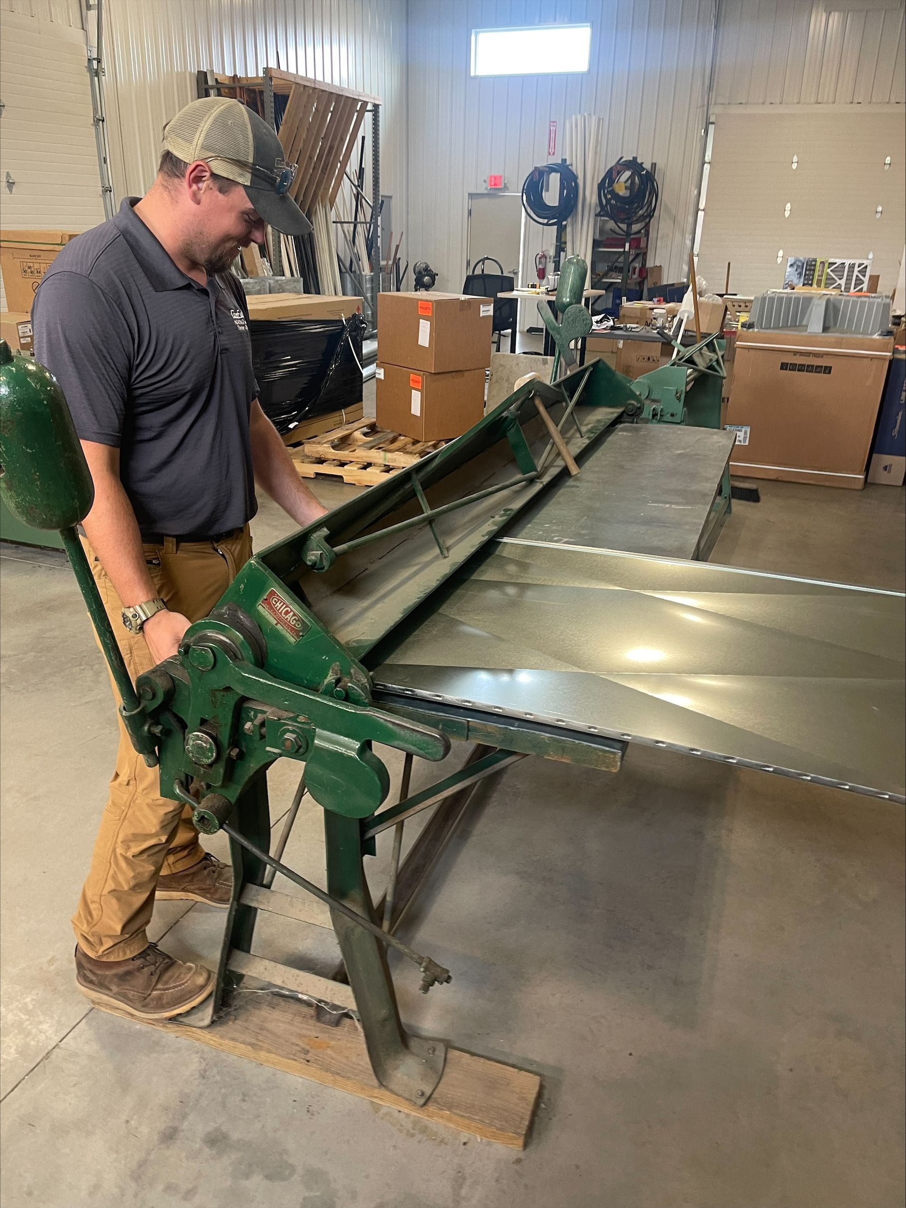 Man operating a green metal sheet brake in a workshop, bending a large sheet of metal.