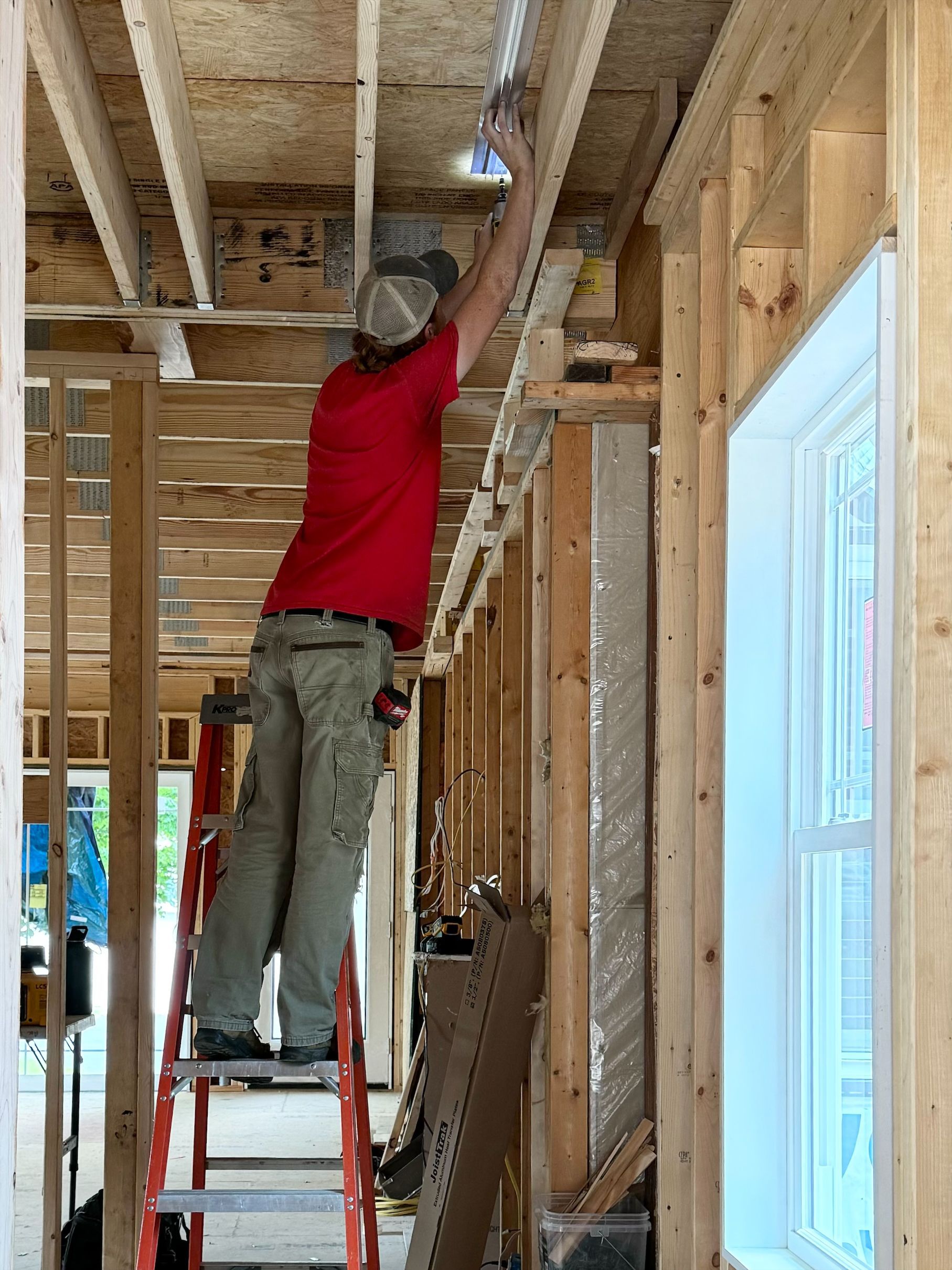 Worker on a red ladder installing ceiling framing in a house under construction