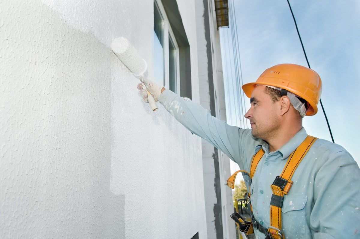 A construction worker in a safety harness paints the exterior of a building with white paint.
