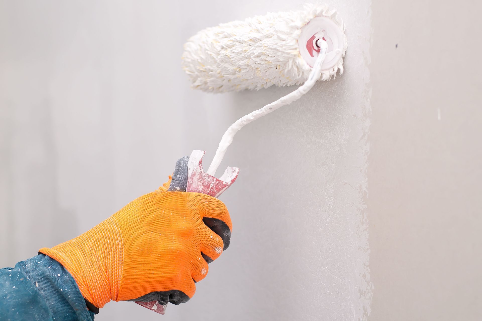 A gloved hand uses a paint roller to apply white paint to a wall.