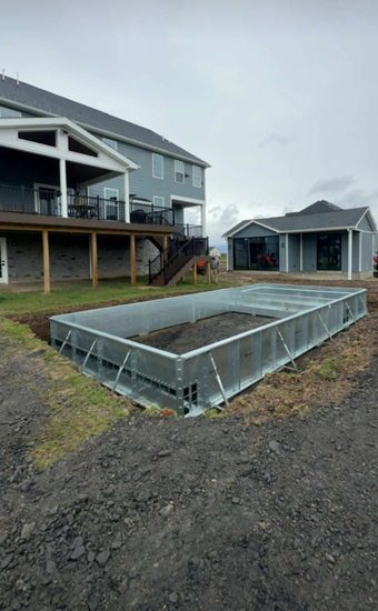 A rectangular, metal pool frame is set in a backyard with a house and shed in the background.
