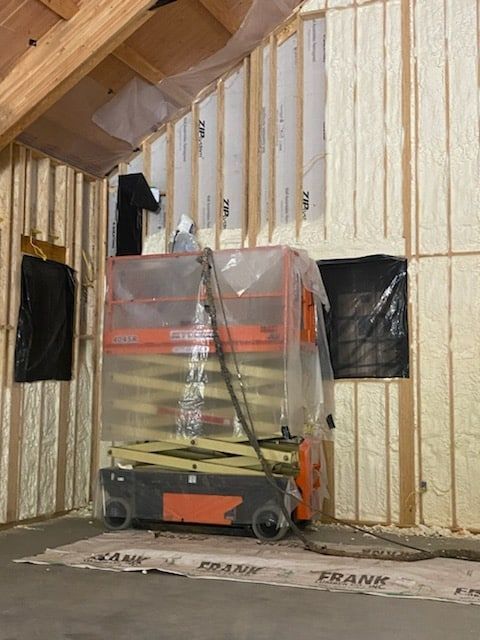 A scissor lift is wrapped in plastic in a room under construction.