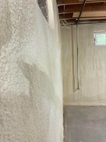 A basement with a wall covered in spray foam and a window.