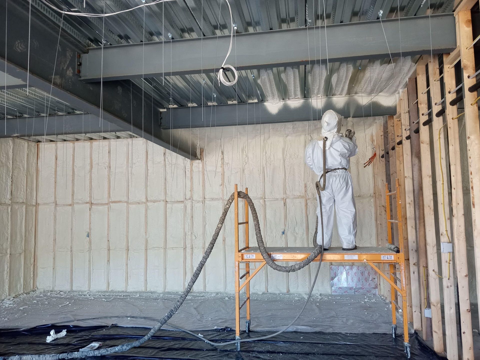 A man in a protective suit is spraying insulation on the walls of a building.